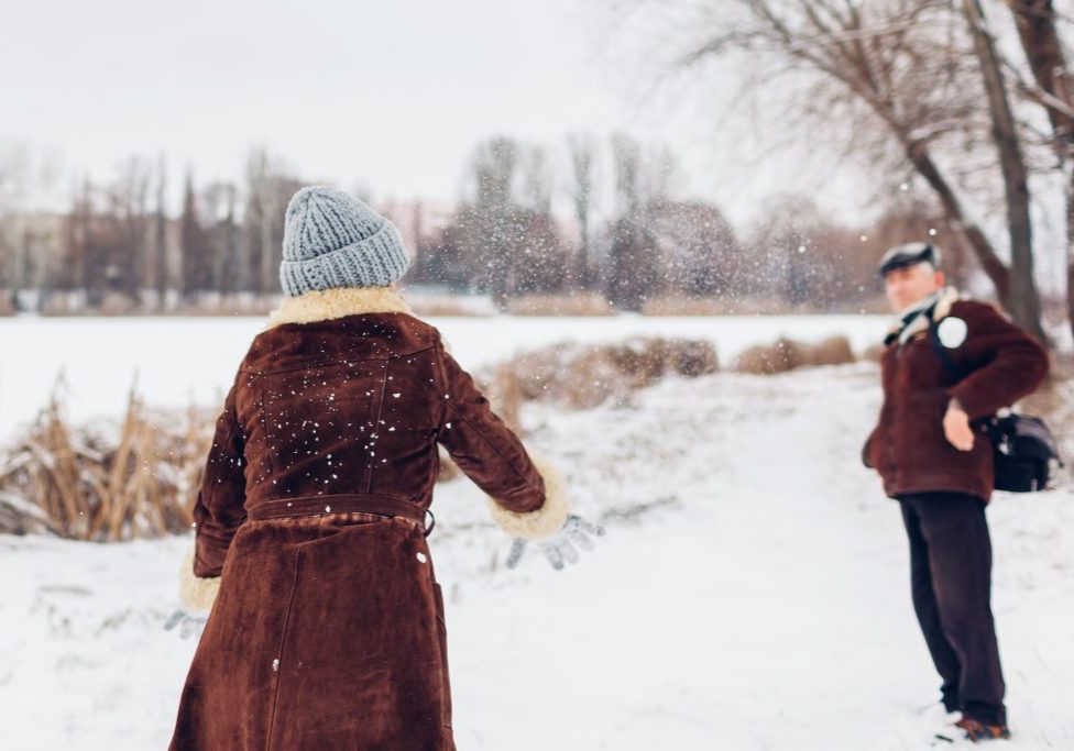 Senior couple playing snowballs outdoors during snowy winter weather. Elderly people having fun walking. 